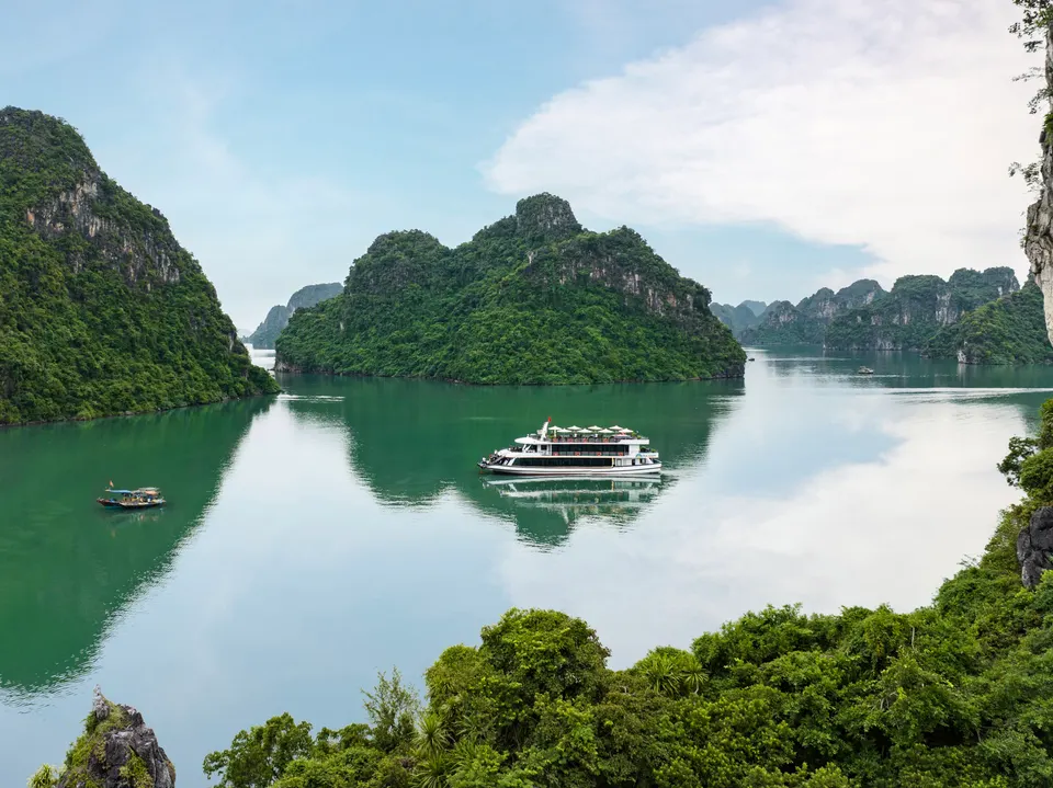 Green limestone islands and a boat on calm water in Lan Ha Bay